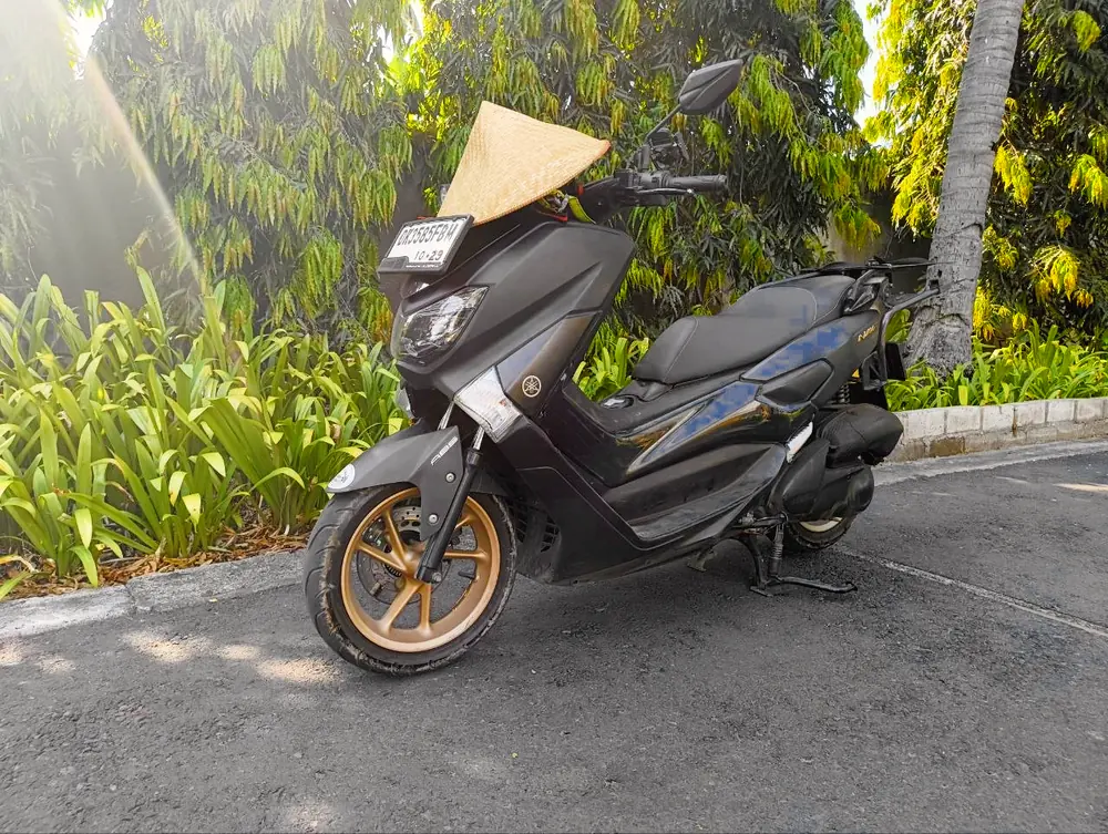 Our black Yamaha NMax 155 with gold wheels and a straw hat on its mirror, parked among green plants